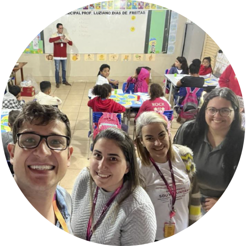 Foto em estilo selfie de um voluntário e três voluntárias do Instituto dentro de uma sala de aula. Todos sorriem.
