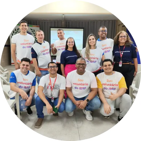 Foto de um grupo de pessoas em uma sala, sendo que parte está em pé e outra abaixada. Todas as pessoas sorriem e usam camisetas do programa de voluntariado do Instituto BRF.