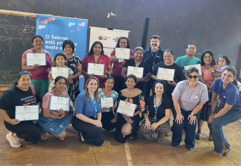 Um grupo de pessoas, em sua maioria mulheres indígenas, posando para a foto, sorrido e exibindo o certificado de conclusão do curso.