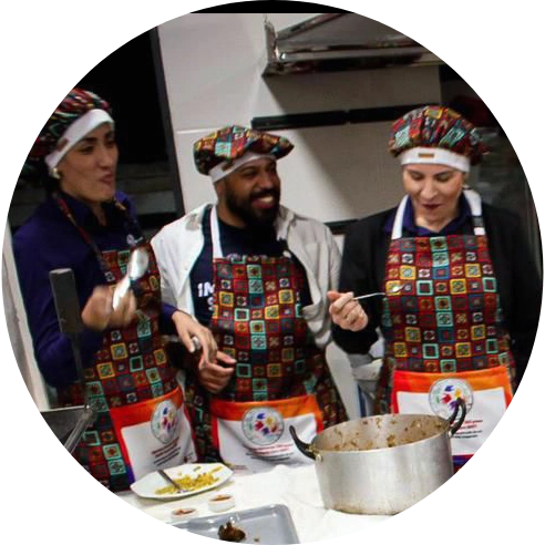 Foto de duas pessoas voluntárias e do analista de impacto social do Instituto IBRF, Caique Silva, em uma cozinha. Eles estão com aventais e toucas coloridas. 