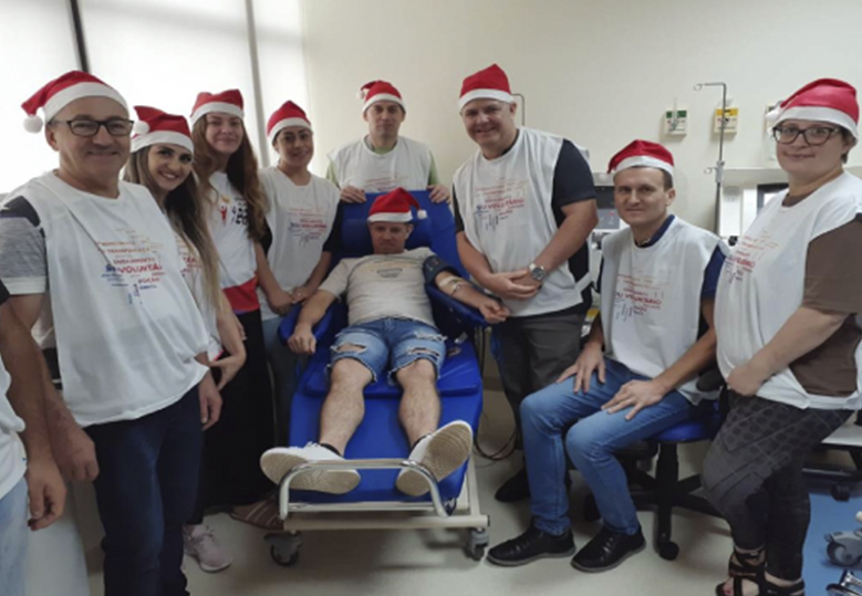 Foto de um grupo de voluntárias e voluntários do Instituto BRF com gorros natalinos ao redor de uma maca onde um deles faz a doação de sangue.