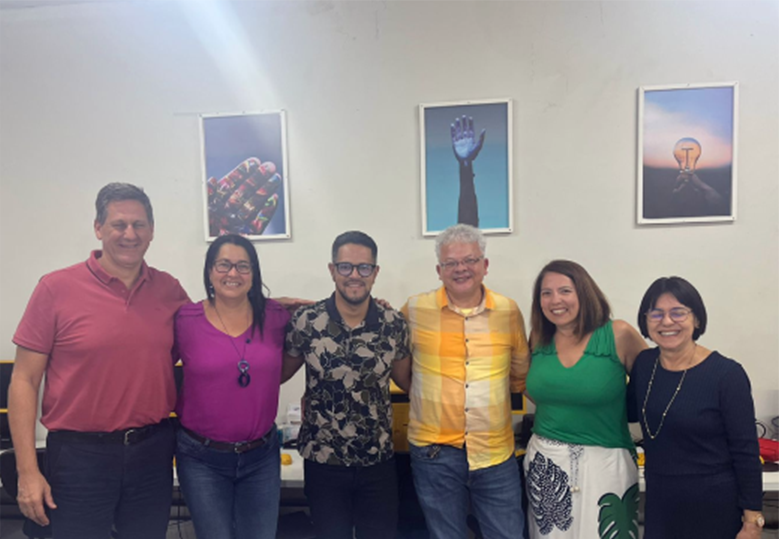Foto de um grupo diverso de pessoas em pé em uma sala. Todos sorriem.