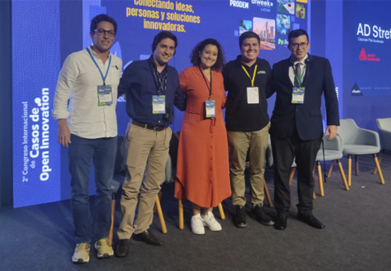 Foto de de Jennifer França com mais quatro homens em cima do palco do evento. Todos estão bem próximos uns dos outros e sorriem.